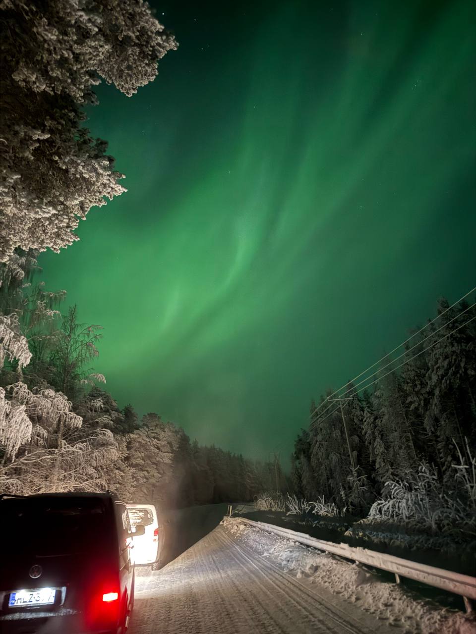 Minibus on a snowy forest road under the aurora