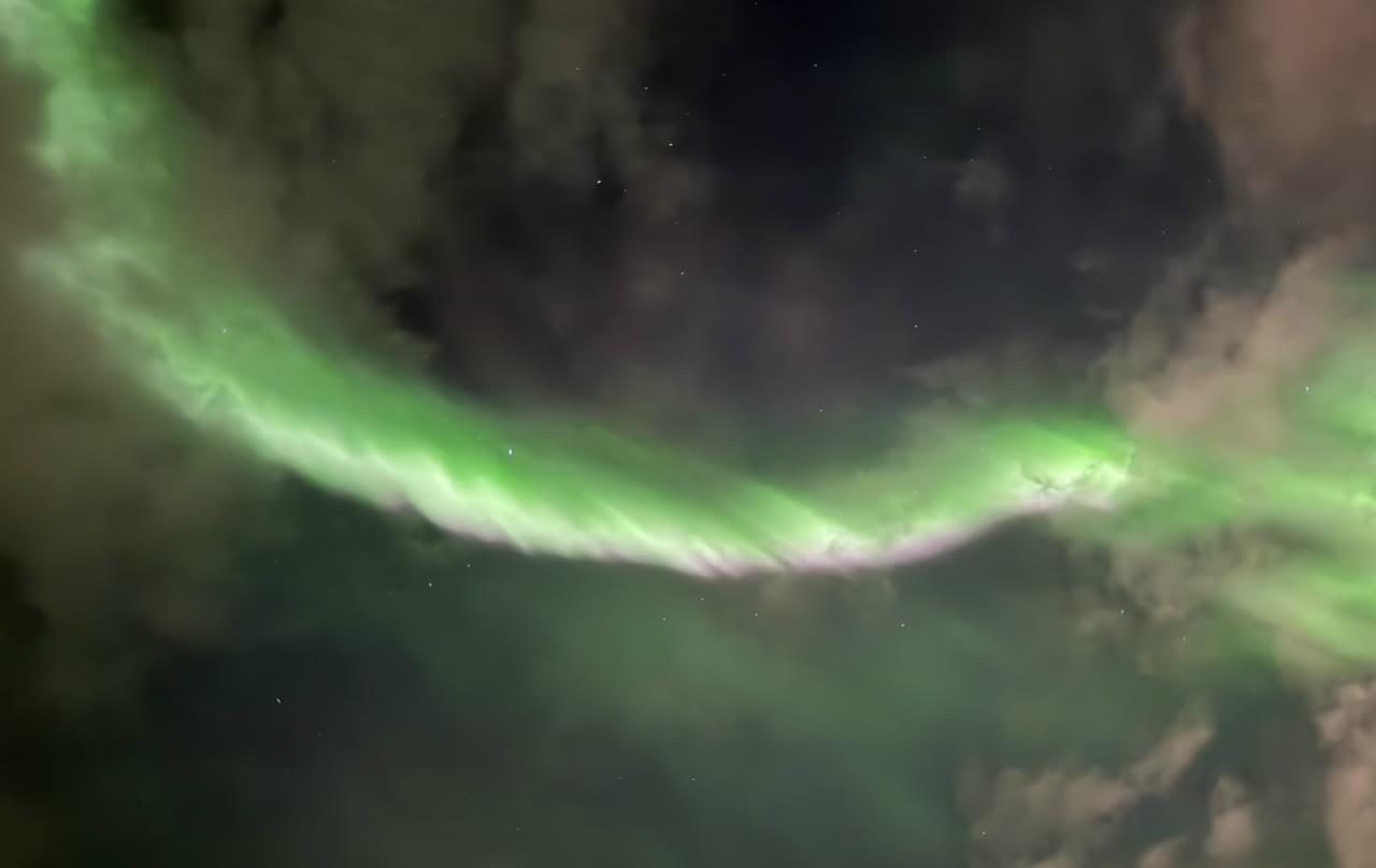 Green arc of aurora through the clouds