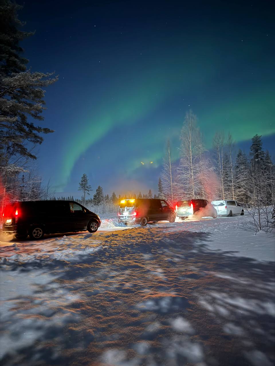 Minibuses parked in the snow under the aurora