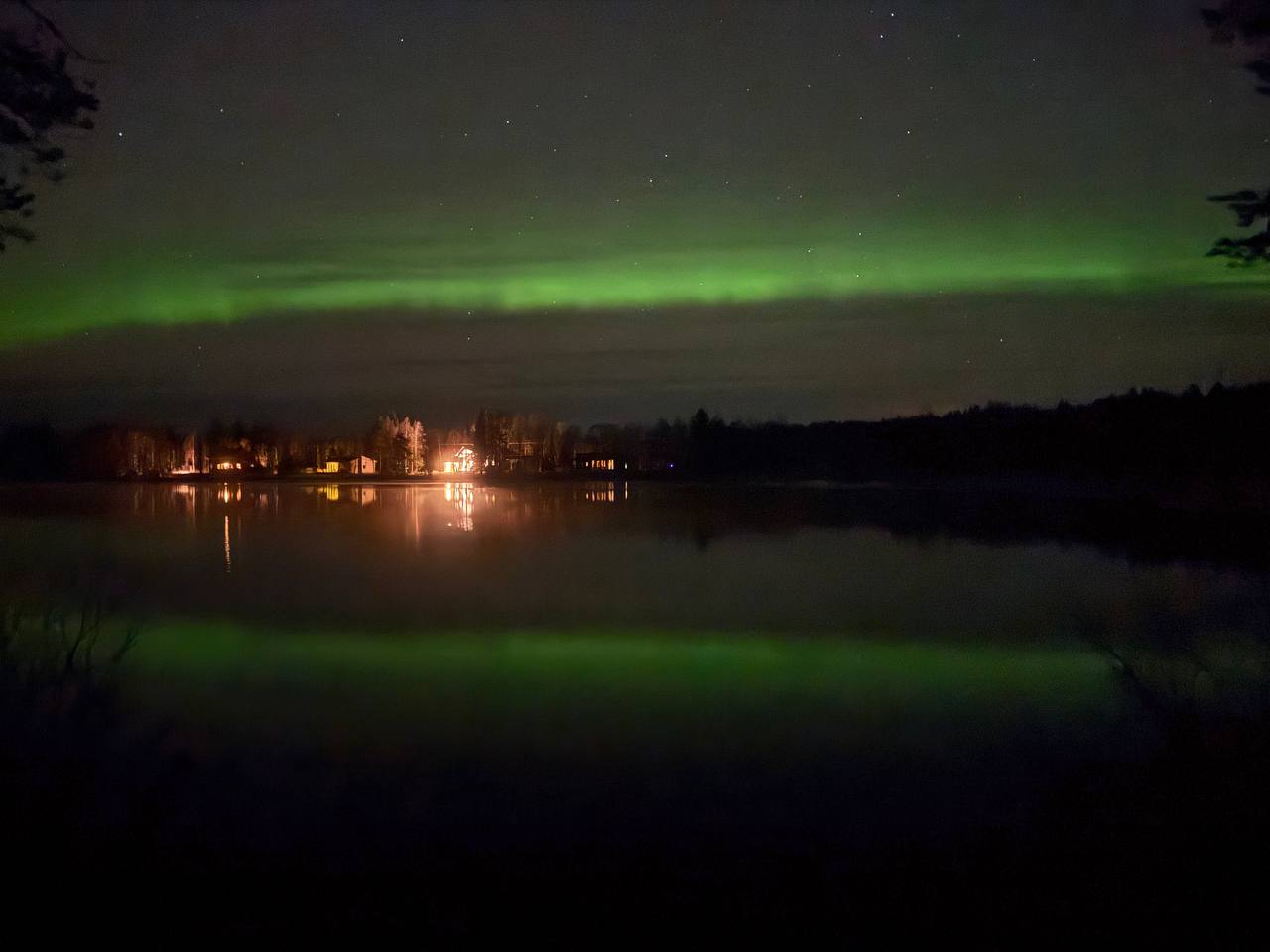 Green aurora over a lake with lights of houses reflected in the water