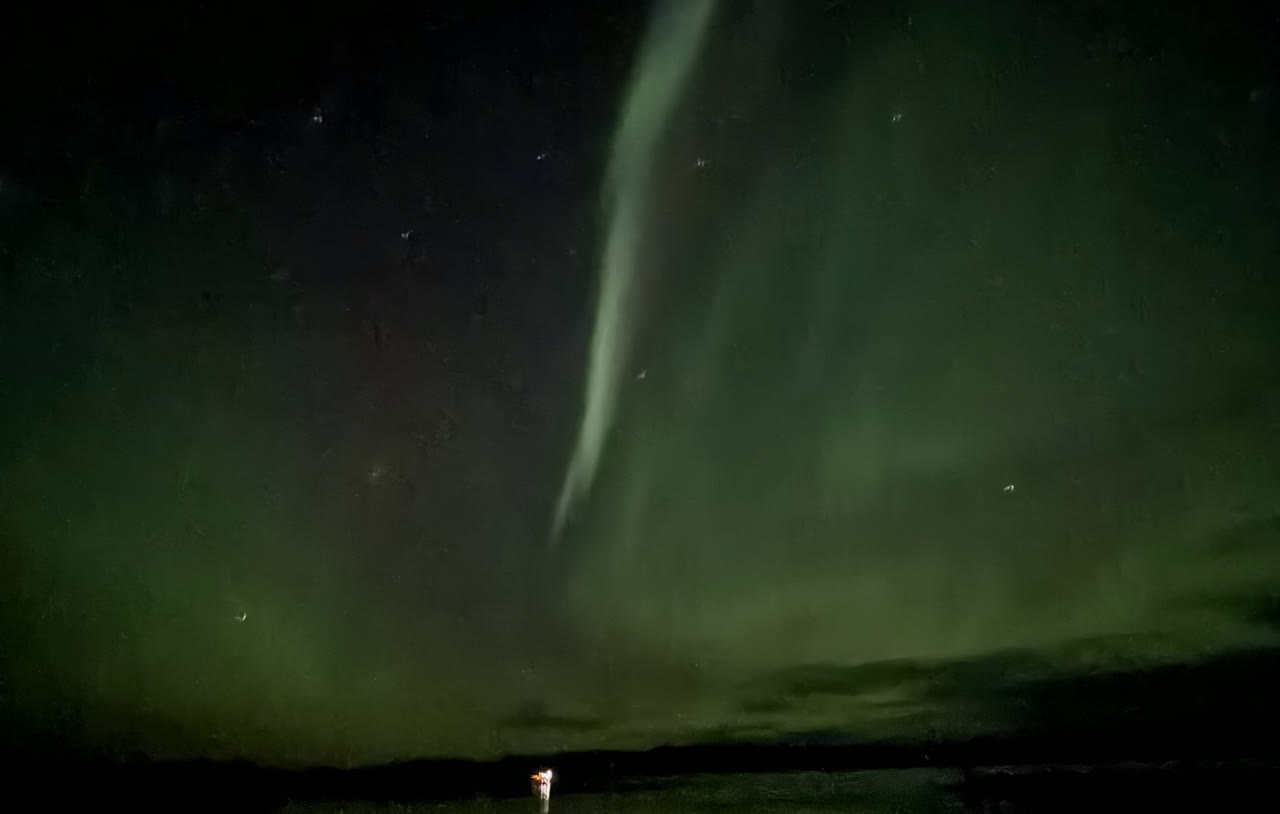 A band of aurora over a lake with a small figure holding a light
